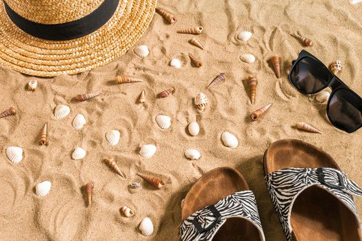 Summer beachwear, flip flops, hat, sunglasses and seashells on sand beach. Top view. Copy space