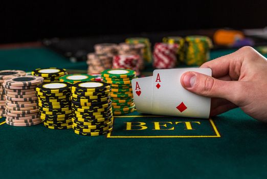 Close-up of male poker player lifting the corners of two cards aces at green casino table with aces