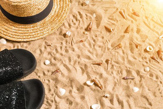 Summer beachwear, flip flops, hat and seashells on sand beach. Top view. Copy space. Sun flare