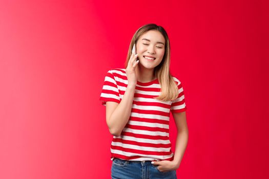 Carefree friendly good-looking blond asian girl having funny conversation, talking phone, close eyes joyfully smiling calling friend hold smartphone near ear, laughing over hilarious voice message.