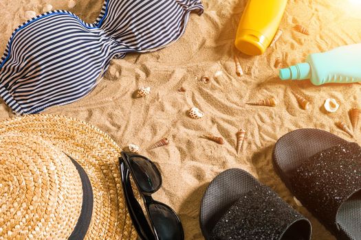 Summer bikini and accessories stylish beach set, Beach bikini summer outfit and sea sand as background, Top View, Concept. Copy space. Sun flare