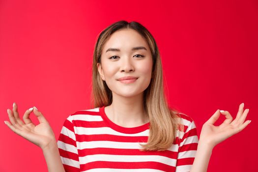 Peaceful happy relaxed asian woman meditating, hold hands zen show orbs sign smiling delighted relieved, feeling patience joy practicing yoga, calm down relaxing, standing red background.