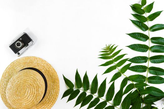 Straw hat with green leaves and old camera on white background, Summer background. Top view. Copy space. Still life. Flat lay