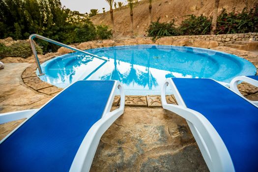 Sunloungers and beautiful swimming pool with reflected of palm trees in a blue water, Egypt.