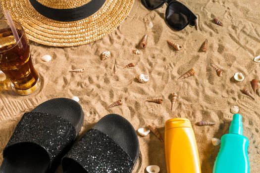 Summer beachwear, flip flops, hat, cold drink in a glass and seashells on sand beach. Top view. Copy space. Still life mockup flat lay