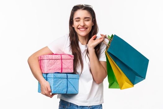 Shopping, holidays and lifestyle concept. Portrait of cheerful excited young woman smiling as likes making presents for friends, close eyes imaging how she give gifts, hold shop bags.