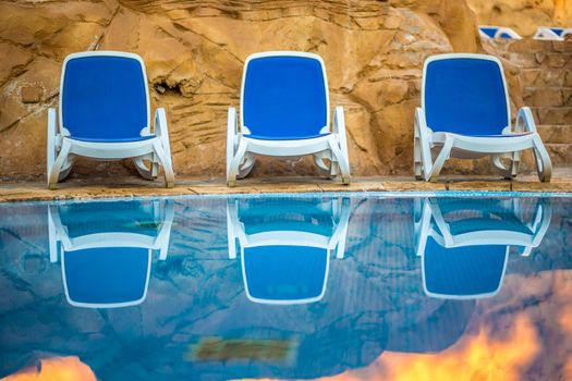 Three sunloungers near beautiful swimming pool and reflected their in a blue water of the pool. Exotic vacation in Egypt.
