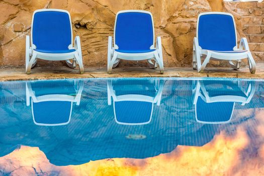 Three sunloungers near beautiful swimming pool and reflected their in a blue water of the pool. Exotic vacation in Egypt.