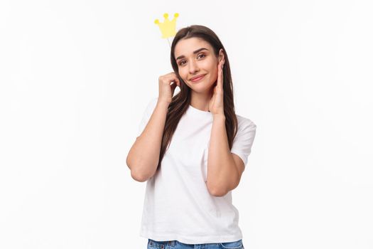 Entertainment, fun and holidays concept. Portrait of beautiful and self-assured charming young smiling woman holding crown on stick near head, feel like princess or queen, white background.