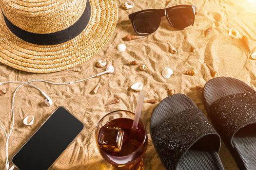 Summer beachwear, flip flops, hat, sunglasses and seashells on sand beach. Top view. Copy space. Sun flare