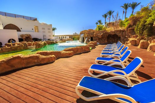 Swimming pool with artificial waterfall and sun loungers, luxury buildings, palm trees, behind it on a beautiful resort in Egypt