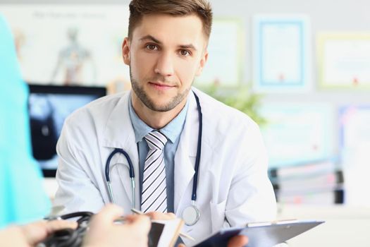 Portrait of attractive young medical worker in white uniform, wait patient for planned appointment. Young specialist in medicine. Healthcare, help concept