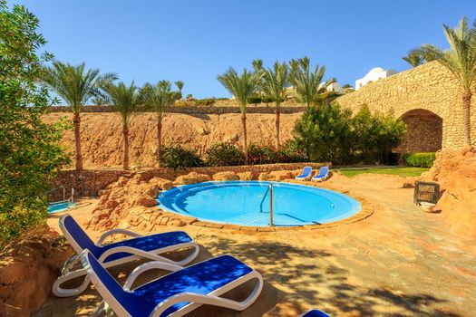 Several of sun loungers by a beautiful swimming pool. Exotic vacation by the hotel pool in bright sunshine, Egypt.