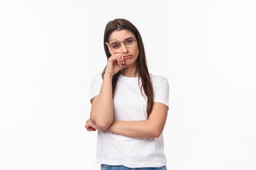 Waist-up portrait of bored, uninterested young brunette female in glasses, feel tired or sleepy, listening to boring conversation, lean on hand look reluctant with lack of interest, white background.