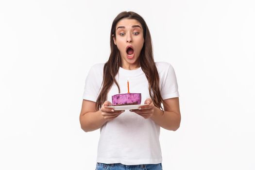 Entertainment, fun and holidays concept. Portrait of funny and cute young caucasian birthday girl making wish, blowing out candle, breathe ait and stare at b-day cake, white background.