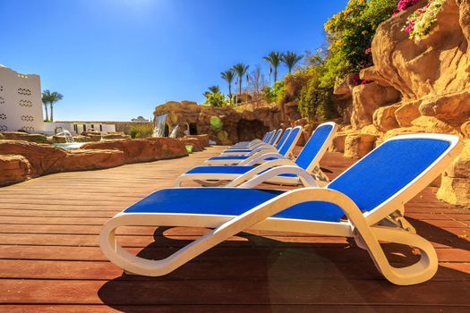 Closeup several of sun loungers by a beautiful swimming pool. Exotic vacation by the hotel pool in bright sunshine, Egypt.