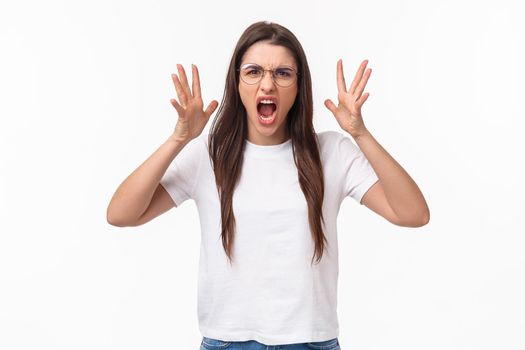 Waist-up portrait of angry, pissed-off brunette pretty girl in glasses, shouting, blaming partner for cheating on her, shaking hands and screaming, having confrontation, frowning aggressive.