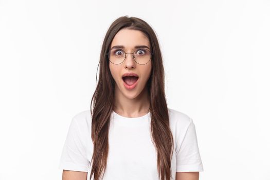 Close-up portrait of enthusiastic, intrigued young brunette woman listening with dropped jaw to amazing news, open mouth fascinated, standing white background, heart great idea, wear glasses.