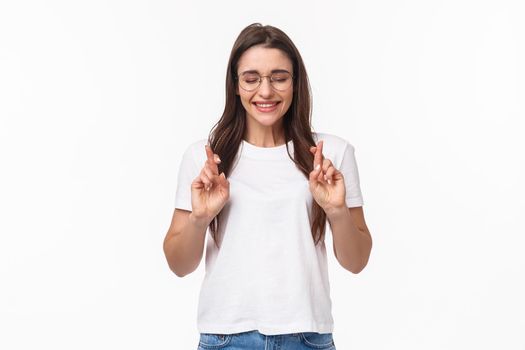 Waist-up portrait of hopeful, excited and optimistic young woman in glasses, cross fingers good luck and close eyes, smiling having faith pleading, making wish, want dream come true.