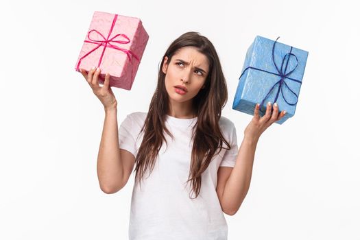 Celebration, holidays and presents concept. Hmmm interesting what inside. Portrait of curious young birthday girl shaking gift boxes trying to understand what friend bought for her, white background.