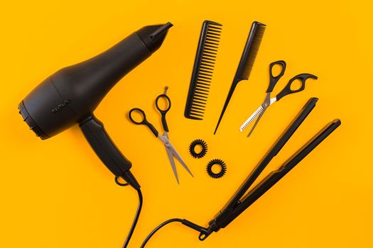 Black hair dryer, comb and scissors on yellow paper background. Top view. Copy space. Still life. Mock-up. Flat lay