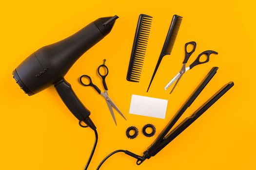 Black hair dryer, comb and scissors on yellow paper background. Top view. Copy space. Still life. Mock-up. Flat lay