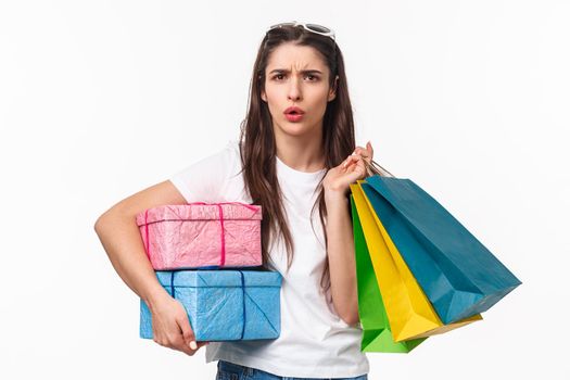 Shopping, holidays and lifestyle concept. Portrait of frustrated and serious young confused woman hear something strange, look concerned or displeased, holding boxes with presents and shop bags.