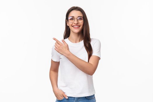 Waist-up portrait of friendly, attractive young 20s woman in glasses, giving advice, recommend try this online shop, click link or visit promo page, pointing finger upper left corner, smile camera.