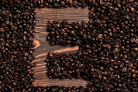 Letter E inscription with coffee bean on the wooden table. Top view. Copy space. Still life. Mock-up. Flat lay