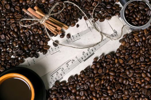 Coffee beans, cinnamon sticks and cup of brewed coffee on sheet music background, view from above with space for text. Still life. Mock-up. Flat lay