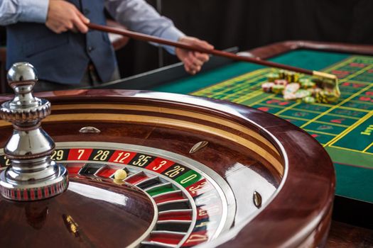 Roulette and piles of gambling chips on a green table in casino. Croupier collects chips using stick