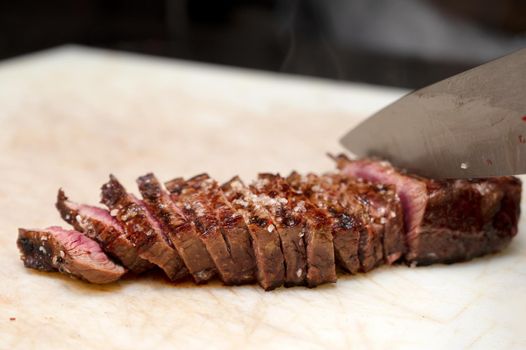 Chef cutting juicy steak on a board at commercial kitchen. High quality photo