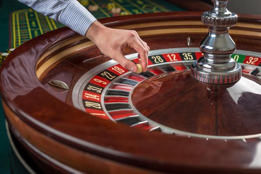 Roulette wheel and croupier hand with white ball in casino close up details