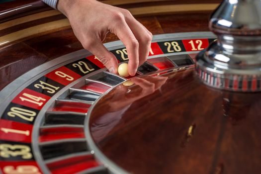 Roulette wheel and croupier hand with white ball in casino close up details