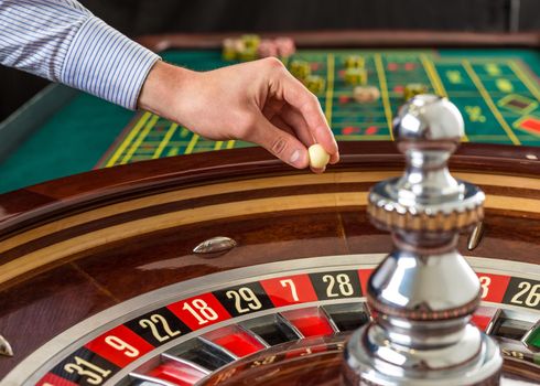 Roulette wheel and croupier hand with white ball in casino close up details