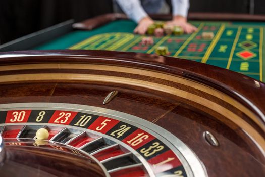 Roulette and piles of gambling chips on a green table in casino. Man hand over casino chips - bet.