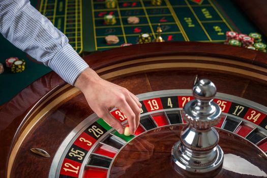 Roulette wheel and croupier hand with white ball in casino close up details