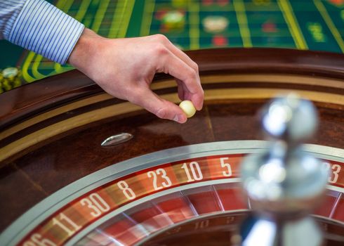 Roulette wheel and croupier hand with white ball in casino close up details