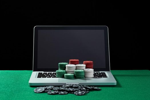 Image of casino chips on a keyboard notebook at green table. Concept for online gambling, poker, virtual casino.