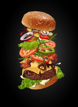 Delicious maxi burger with flying ingredients against black background. Ham, beef cutlet, cheese, mayonnaise, vegetables and greens. Cooking, fast food. Unhealthy nutrition. Close up, copy space
