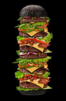 Huge appetizing black burger on black background. Ham, beef cutlet, cheese, vegetables and greens. Concept of cooking and fast food. Unhealthy nutrition. Close up, copy space