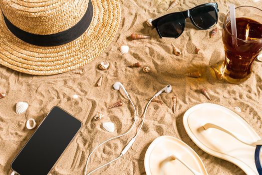 Summer beachwear, flip flops, hat, sunglasses and seashells on sand beach. Top view. Copy space