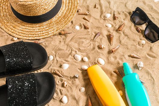Summer beachwear, flip flops, hat, sunglasses and seashells on sand beach. Top view. Copy space