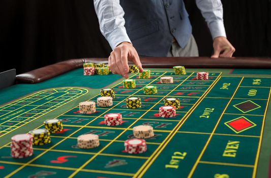 Picture of a green table and betting with chips. Man hand over casino chips on roulette table. Close up