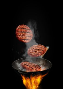 Wok pan with smoke above fire is frying three beef cutlets against black studio background. Cooking concept. Close up, copy space