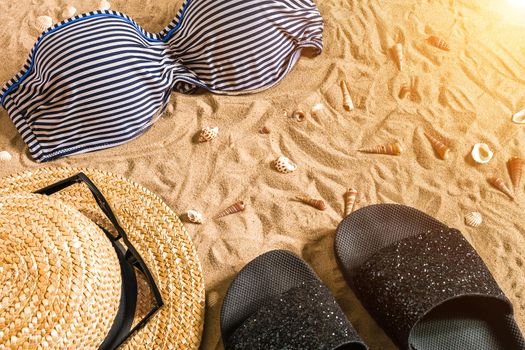 Summer bikini and accessories stylish beach set, Beach bikini summer outfit and sea sand as background, Top View, Concept. Copy space. Sun flare