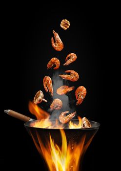 Wok pan with smoke above fire is frying some shrimps with garlic against black studio background. Cooking concept. Close up, copy space