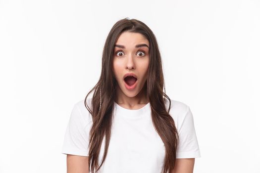 Close-up portrait of surprised and startled young brunette female drop jaw from spilled tea, gossiping and hear something incredible, open mouth fascinated looking camera impressed.