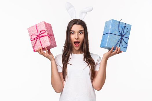 Celebration, holidays and presents concept. Portrait of charismatic young woman in lovely rabbit ears, shaking two gift box and look camera with opened mouth and surprised expression, receive present.