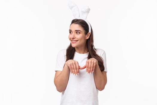 Portrait of funny and cute, playful adult girl in t-shirt and rabbit ears, look away with amused happy face, imitating bunny with paws and silly grin, look away, standing white background.